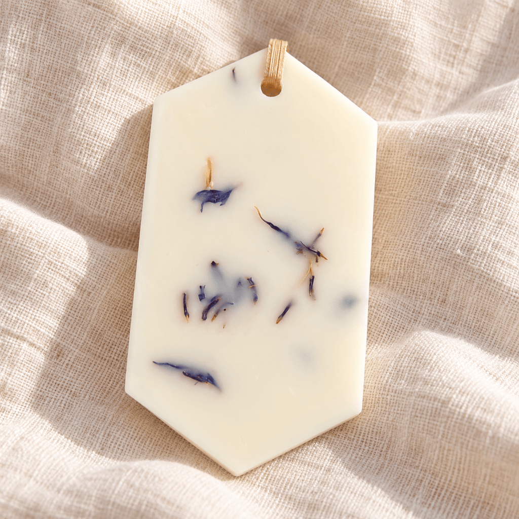 Odorizant pentru dulap din ceară naturală, decorat cu flori uscate albastre, cu parfum de zambile și așezat pe o pânză textilă ivory.